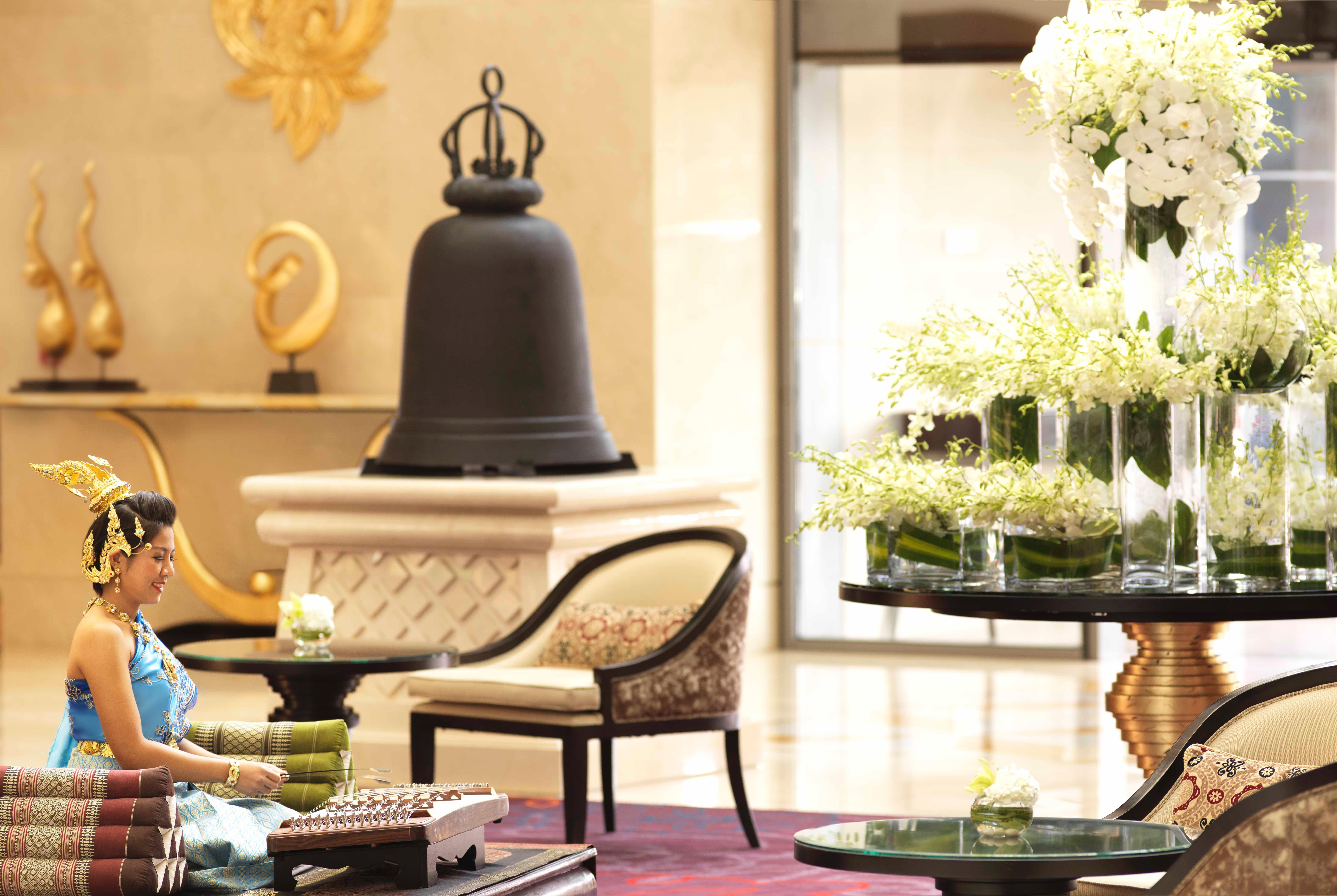 Dusit Thani Абу-Даби Экстерьер фото The photo depicts an elegant lobby setting. In the foreground, a woman is seated on a chair, surrounded by neatly arranged colorful towels. She appears to be engaged in an activity or simply enjoying the ambiance. 

In the background, there is a larg