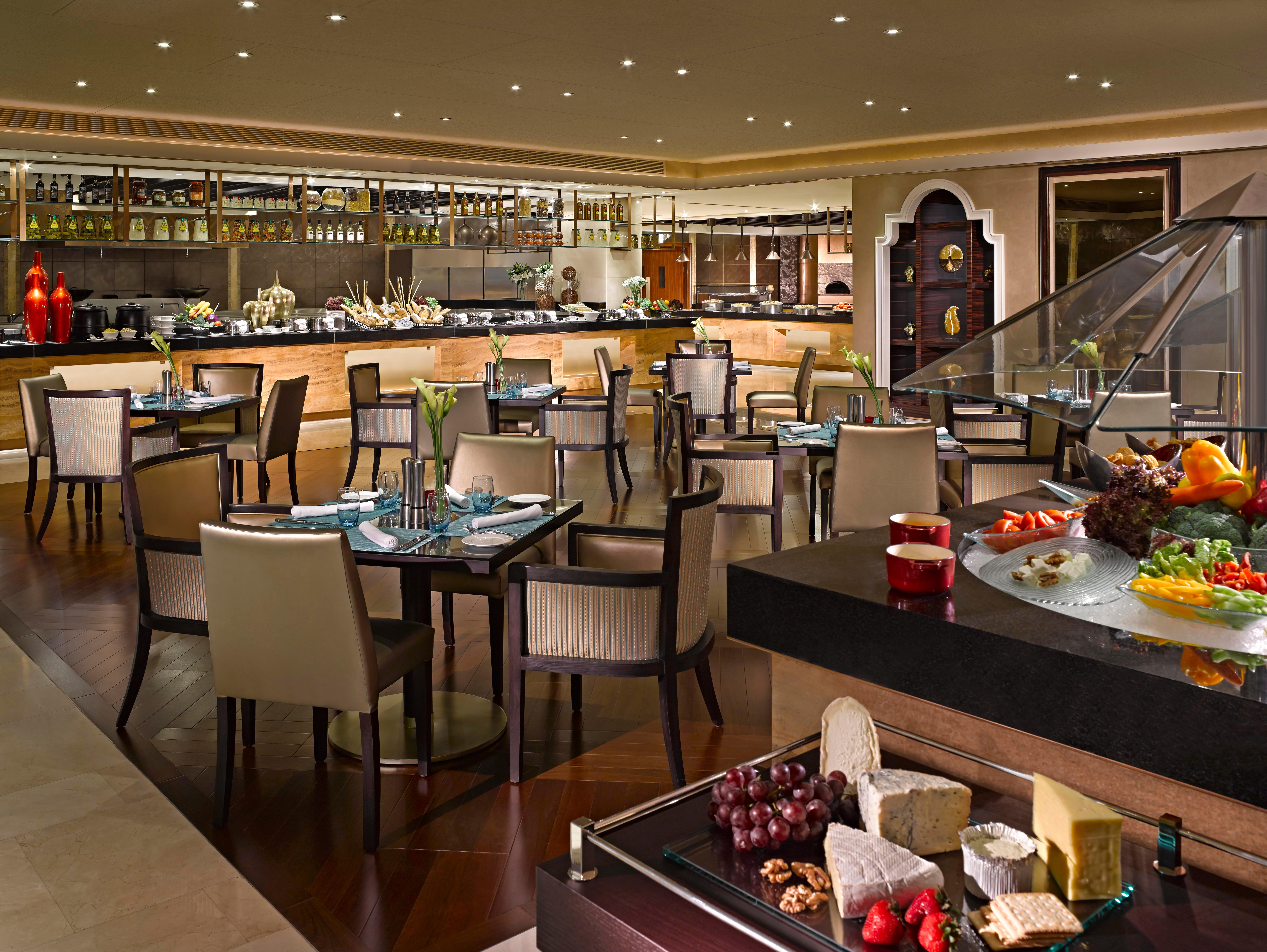 Dusit Thani Абу-Даби Экстерьер фото The photo depicts a spacious and elegantly designed restaurant interior. It features a mix of wooden and modern furnishings, including numerous tables and chairs arranged throughout the dining area. On one side, there is a buffet setup with a variety
