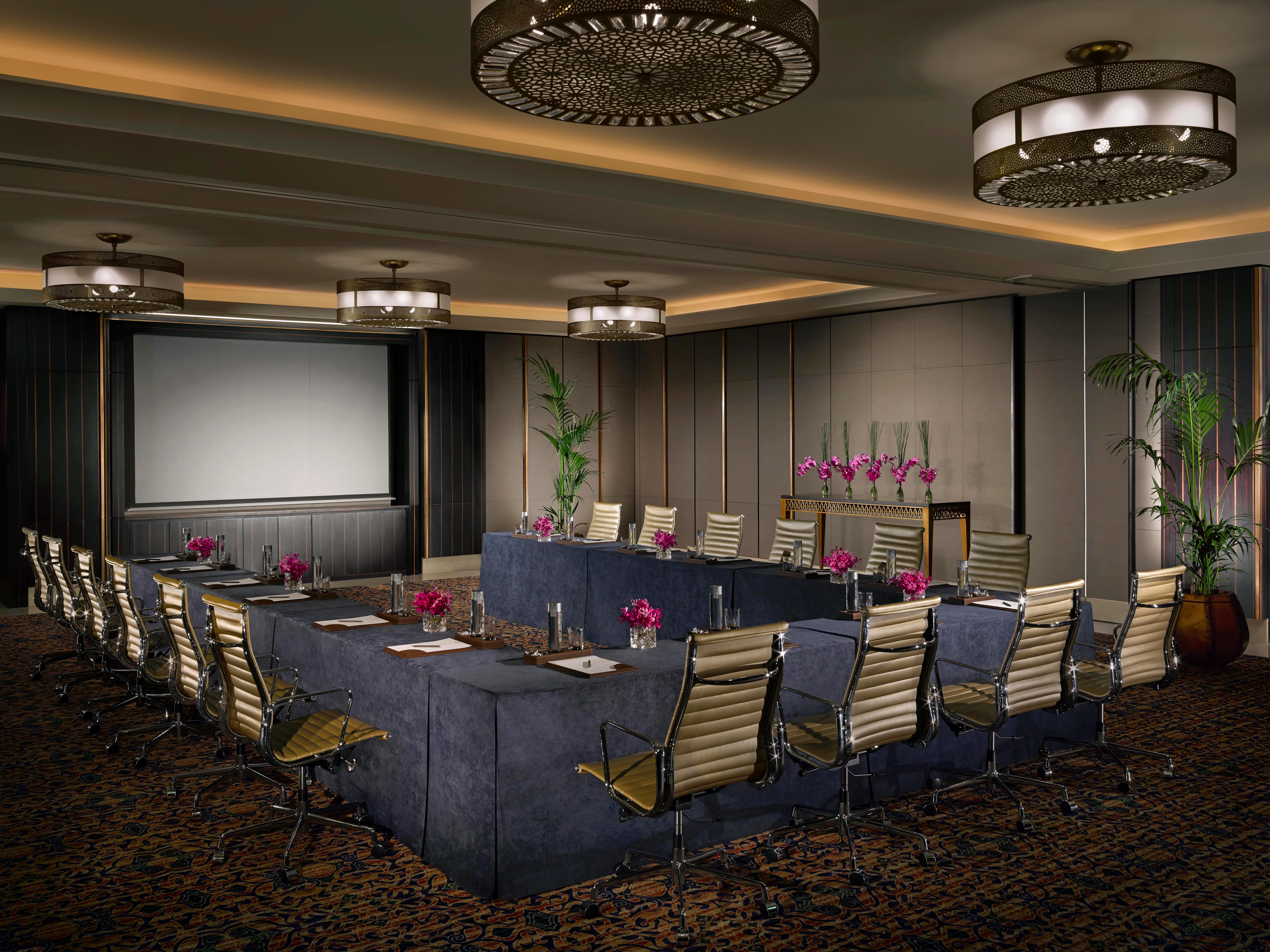 Dusit Thani Абу-Даби Экстерьер фото The photo depicts a well-designed conference room. It features a large, rectangular table arranged with several ergonomic chairs around it. The room is illuminated by stylish overhead light fixtures, and there is a large screen at one end for present