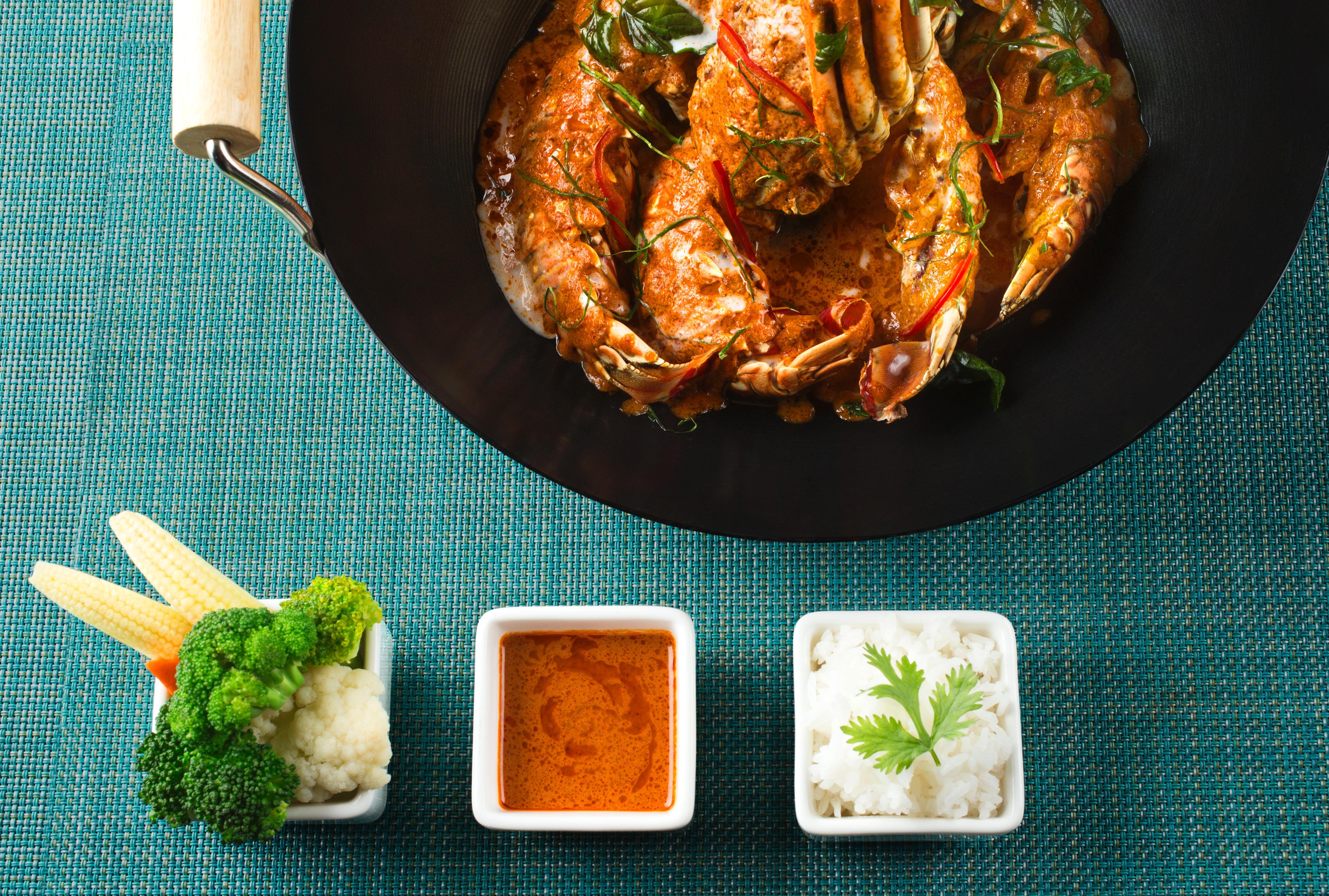 Dusit Thani Абу-Даби Экстерьер фото The photo features a colorful dish of cooked shrimp, presented in a black frying pan. The shrimp appear to be well-seasoned, likely with herbs or spices, and are accompanied by sliced vegetables. Next to the pan, there are three small bowls. One bowl