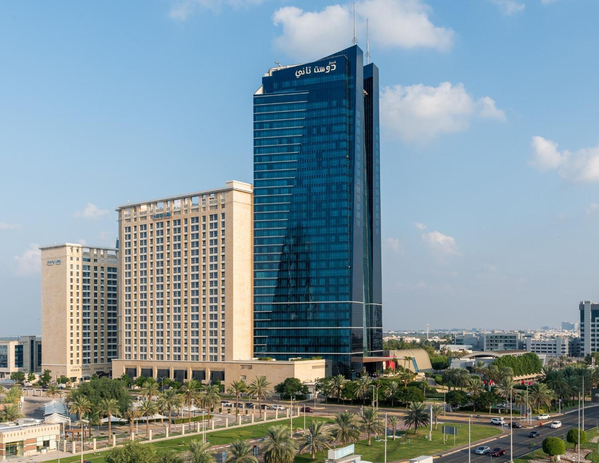 Dusit Thani Абу-Даби Экстерьер фото The photo shows two modern buildings in a clear outdoor setting. The taller building on the right has a sleek, reflective glass facade and is designed with contemporary architecture, while the shorter building on the left appears to be more tradition